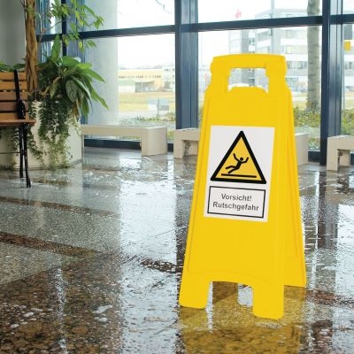 Gelber Warnaufsteller mit Warnsymbol und Text Vorsicht Rutschgefahr auf feuchtem Bodem